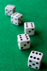 Top view of dice with the number six in the foreground focused, and four dice in bokeh in the background on green mat, in vertical