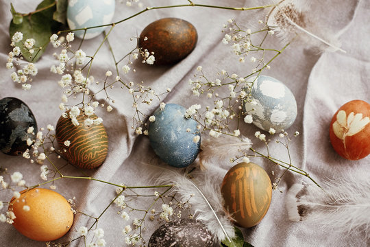 Happy Easter. Stylish easter eggs on rustic table. Natural dyed colorful easter eggs with spring white flowers and feathers on rural textile background. Flat lay