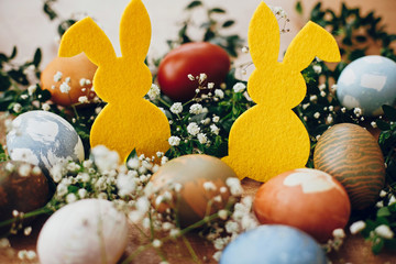Happy Easter. Stylish easter eggs, yellow bunny in nest of spring flowers on rustic wooden table,...