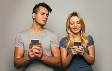 Let me see. Close-up photo of a serious man, who is looking up in the smartphone of his happy girlfriend, reading what she is searching for there.