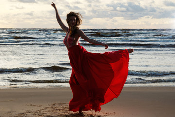 Stunning woman wearing beautiful red dress on the beach