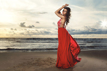 Stunning woman wearing beautiful red dress on the beach