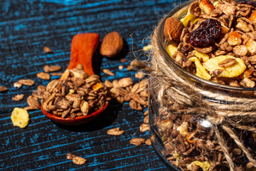 Granola with almonds and dry berries in a glass jar on a blue background.