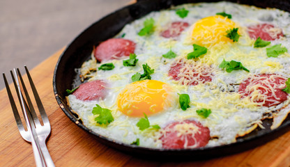 fried egg with ham sausage and cheese in a frying pan on wooden table background