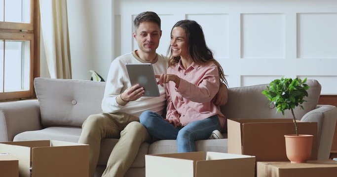 Happy couple using tablet talking on sofa on moving day