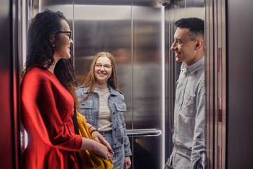 The girls and the guy ride in the elevator. Students in the elevator go to study. People in the elevator. Elevator with people, communication in public places. Colleagues go to work in the elevator.