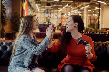Two girlfriends play video games, holding joysticks in their hands. Console games, addiction,...