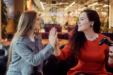 Two girlfriends play video games, holding joysticks in their hands. Console games, addiction, streamers. The girls won the video game, give five, laugh. Female power, victory, joy.