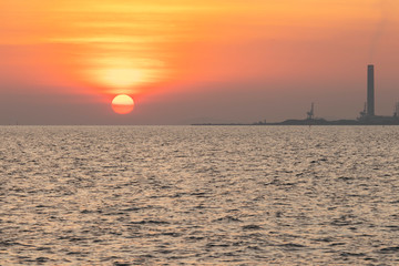 The red sun over the evening sea near the industrial area by the sea