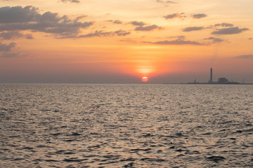 Fototapeta premium The red sun over the evening sea near the industrial area by the sea