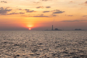 Fototapeta na wymiar The red sun over the evening sea near the industrial area by the sea