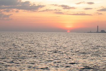Fototapeta premium The red sun over the evening sea near the industrial area by the sea