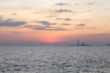Obraz premium The red sun over the evening sea near the industrial area by the sea