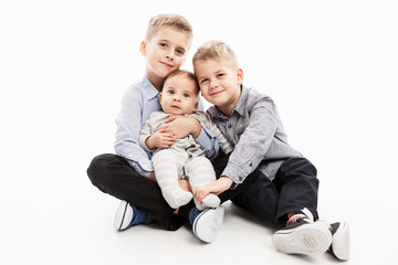 Two brothers are holding a newborn and smiling. Love and tenderness in the family. White background.