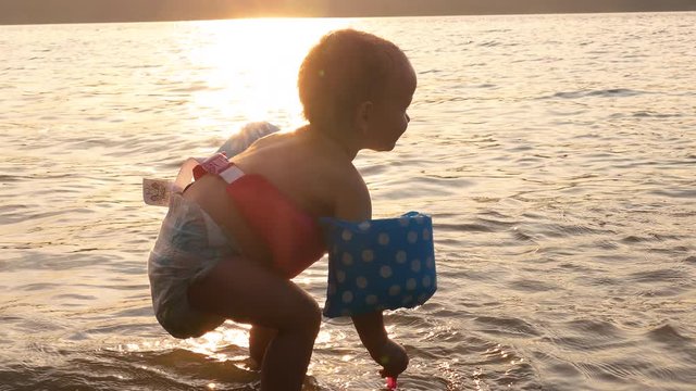 Toddler Playing in lake Water at Sunset Wearing Diaper and Life Jacket