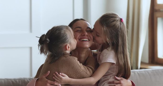 Two small cute daughters hugging kissing happy mama on cheeks
