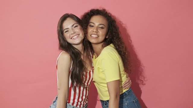 Two happy pretty girls friends having fun together and looking at the camera over pink background