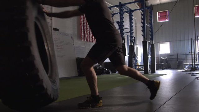 Man picking up and flipping big tire in gym as he works on strength exercises.