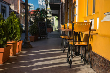Empty chairs of summer cafe standing outside on the street in historical part of touristic European city old center, Morning light.