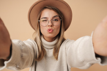 Portrait of pleased young woman in hat winking and taking selfie