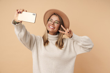 Portrait of woman gesturing peace sign and taking selfie on cellphone