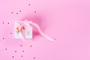 Gift or present box with confetti stars and pink ribbon on pastel pink background. Holiday pattern. Flat lay style.