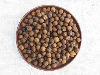Spices and herbs help maintain good health and improve appetite, top view on white concrete background. Allspice in clay plate. Modern apothecary, naturopathy and ayurveda concept.