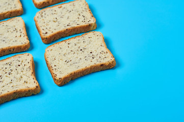 Rows of square pieces of bread with seeds for toast lies on blue table on kitchen. Space for text