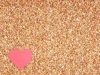 Small red heart on buckwheat groats background. I love buckwheat concept