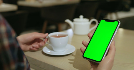 Close up of women's hands holding cell telephone with blank screen in cafe