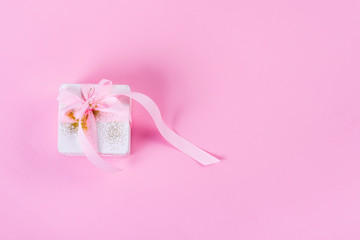 White gift box tied with pink ribbon on pink pastel background with copy space