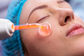 Receiving electric darsonval facial massage procedure at beauty salon