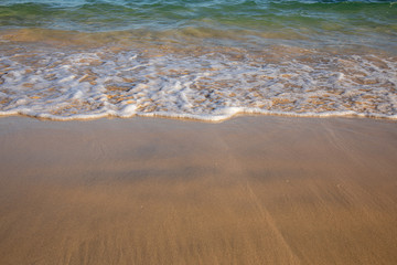 Waves breaking on an empty sand beach and spalsh producing white foam - travel holiday vacation summer season sun splashing water wavy golden yellow sand sandy background blue azure yellow aquamarine