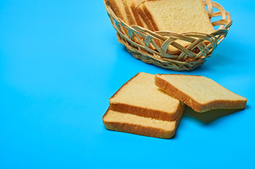 Wooden basket full of square pieces of yellow vanilla bread for toast lies on blue table on kitchen. Space for text