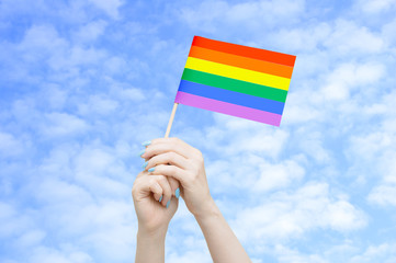 Fototapeta premium Flag LGTB in the hands of a caucasian woman against the sky with clouds.