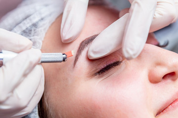 Cosmetic procedures for the treatment of eyebrows. Microblading in the beauty salon. Professional cosmetology. The process of applying the pigment.