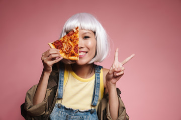 Image of young asian girl wearing white wig having fun and eating pizza
