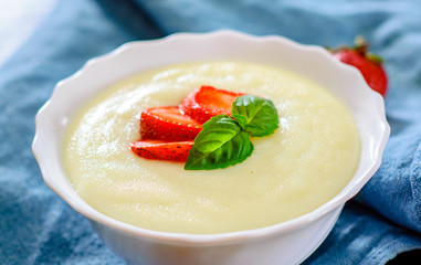 bowl of Semolina porridge with strawberries on wooden table