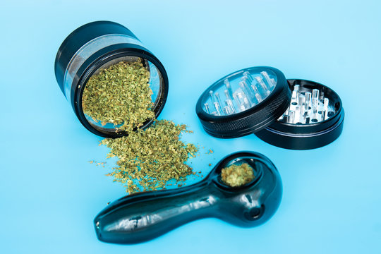 Close up of cannabis - marijuana buds, leaf and accessories - grinder, rolling papers and rolled joint - splif. on blue Background