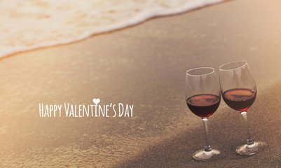Wine glasses with red wine on the beach and words written on sand.. Valentine's Day concept.