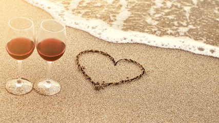 Wine glasses with red wine on the beach and words written on sand.. Valentine's Day concept.