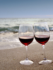 Wine glasses with red wine on sand on the beach. Valentine's Day concept.