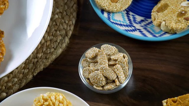 Zoom out shot of beautifully plated Lohri sweets on a wooden table - Happy Lohri. Top view shot of rewri  murmura ladoo  peanuts chikki  and crispy til gajak consumed during the winter season in In...