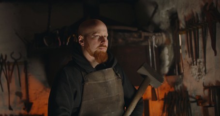 Portrait of a young blacksmith with a big hammer in his workshop