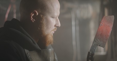 Portrait of a young blacksmith looking at his knife in his workshop