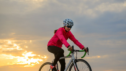 Young Woman Cyclist Riding Road Bike at Sunset. Healthy Lifestyle and Outdoor Sport Concept