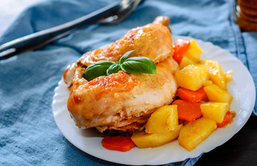 roasted half chicken with carrots, onions and potatoes served on a white plate on table