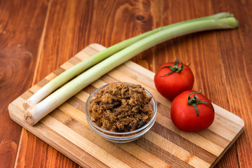 Domestic salty fried Pork greaves, duvan cvarci, in a Glass Bowl with Tomato and Leek on a Cutting Board and on Wooden Table