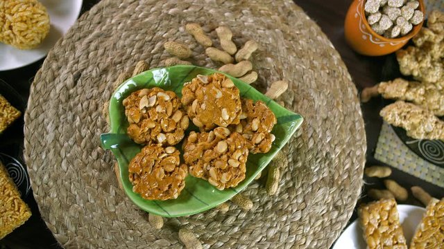 Closeup shot of peanuts chikki with roasted groundnuts - Lohri celebration in India. Beautifully plated peanuts chikki rotating on a turntable and surrounded by rewri  gajak  murmura laddu  etc con...