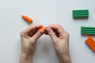 Woman hands putting green color on dot on orange carrot from polymer clay
